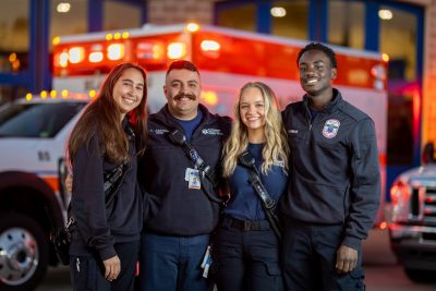 (From left) Sydney Sokol, Andre Asarian, Miranda Jones, and Albert Annan standing in front of a Blacksburg Rescue Squad ambulance with the emergency lights on.