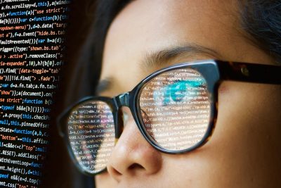 Close-up of a person wearing glasses with computer code reflected in the lenses